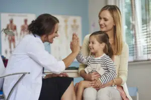 Doctor high-fives a young girl sitting on her mom’s lap at a Family Medicine clinic.